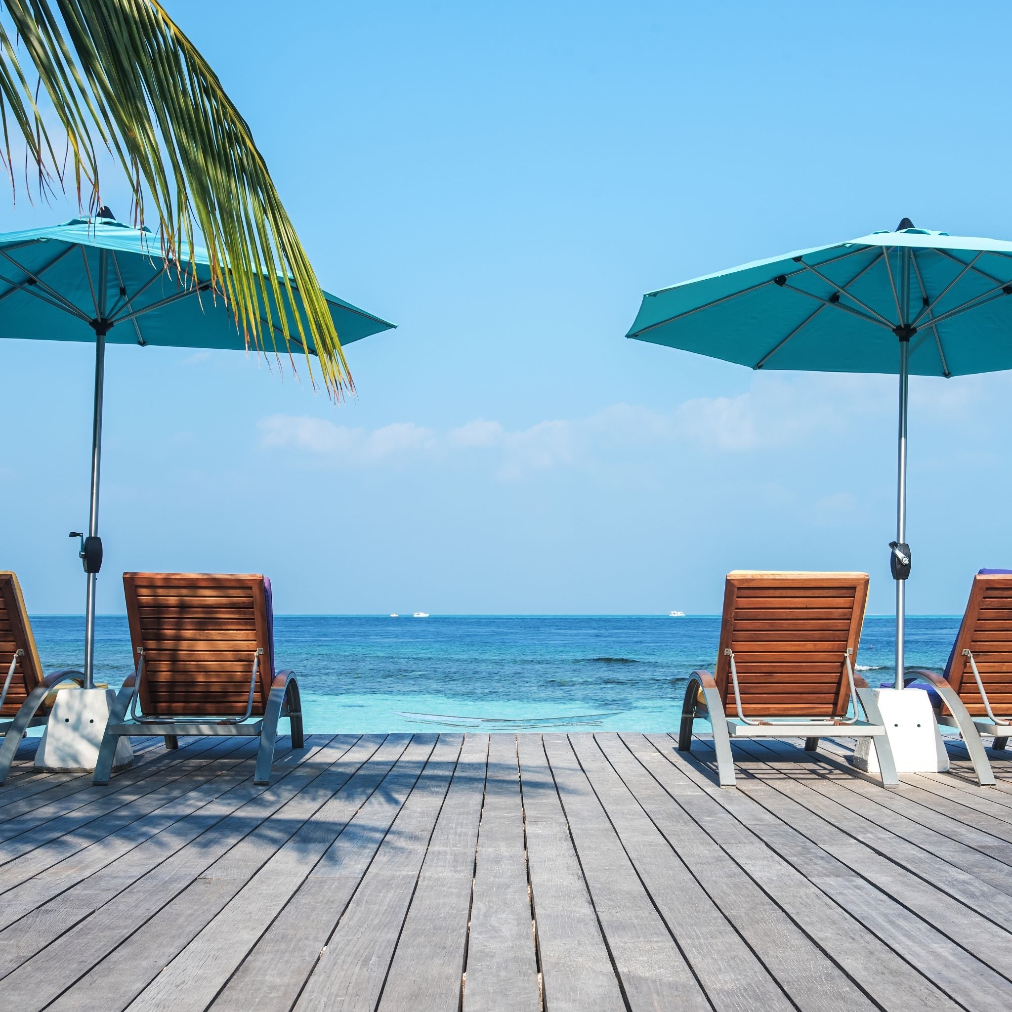 wooden deck with beach reclining beach chairs under umbrellas with a view of the ocean
